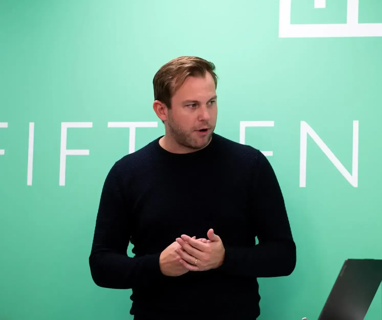 A man stands in front of a green wall that says fifteen