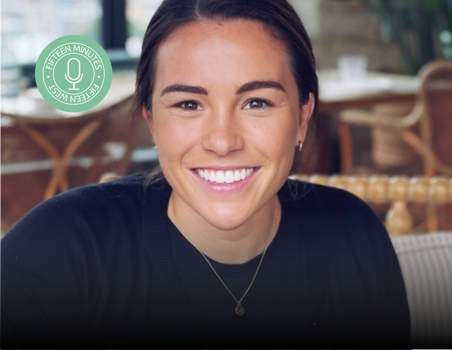 A woman wearing a black shirt and a necklace smiles for the camera
