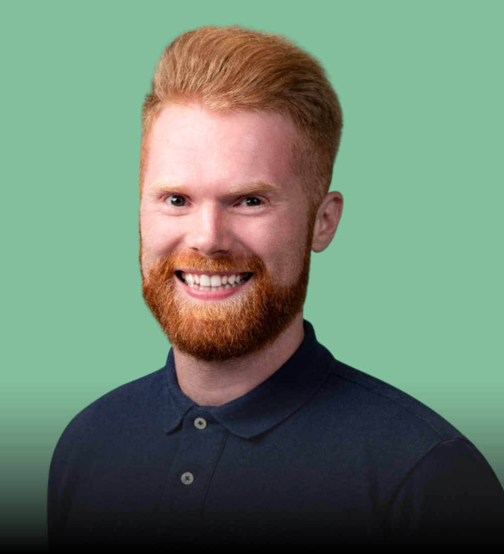 A man with a beard is wearing a blue polo shirt and smiling.
