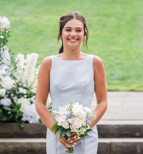 A woman in a light blue dress is holding a bouquet of flowers and smiling.