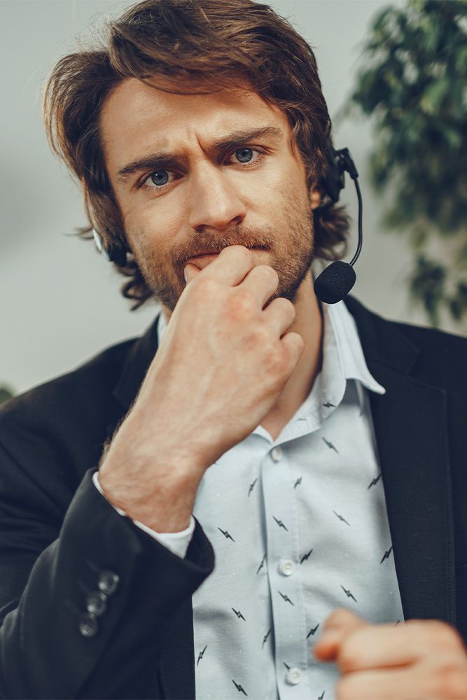 A man wearing a headset is covering his mouth with his hand.