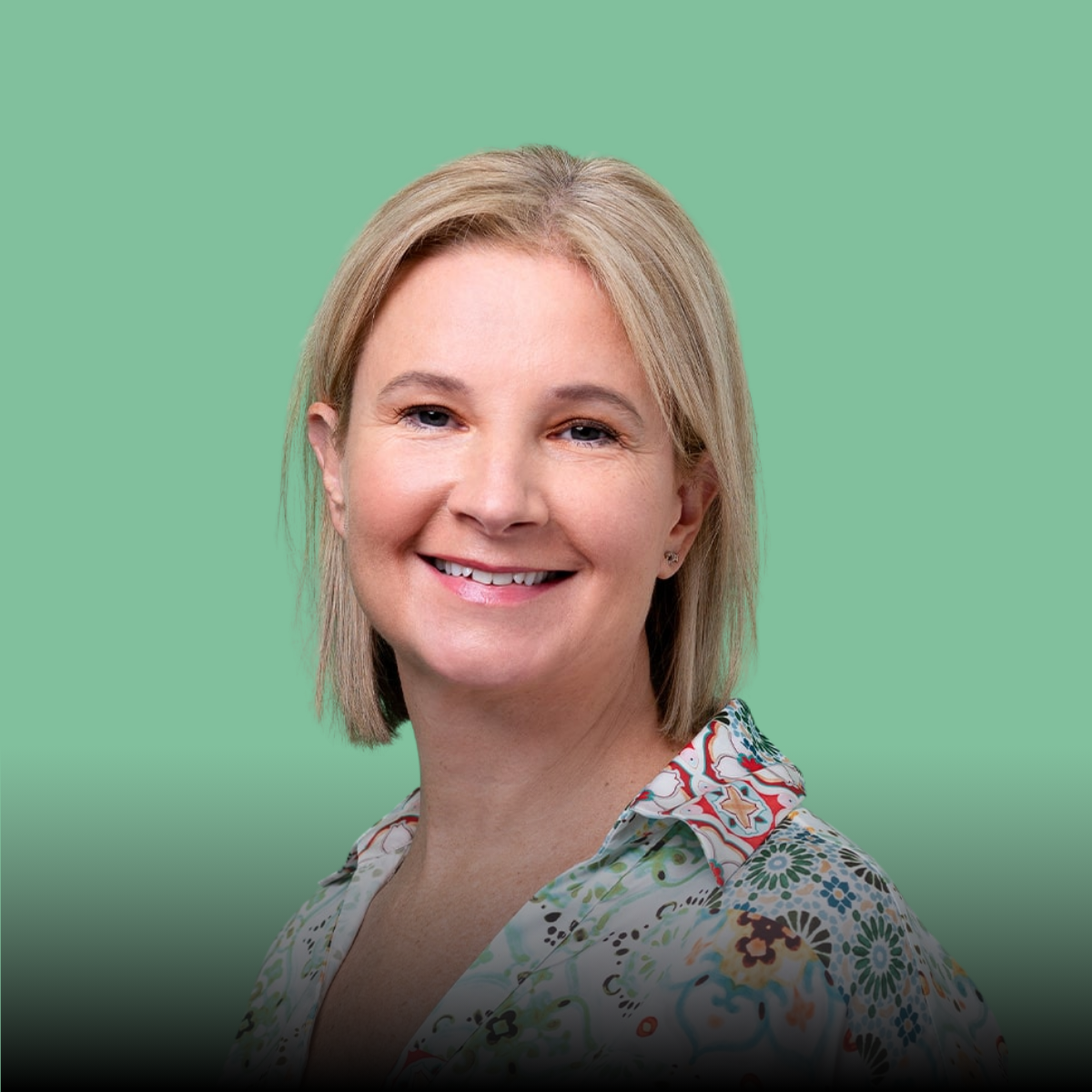 A woman is smiling and wearing a floral shirt on a green background.