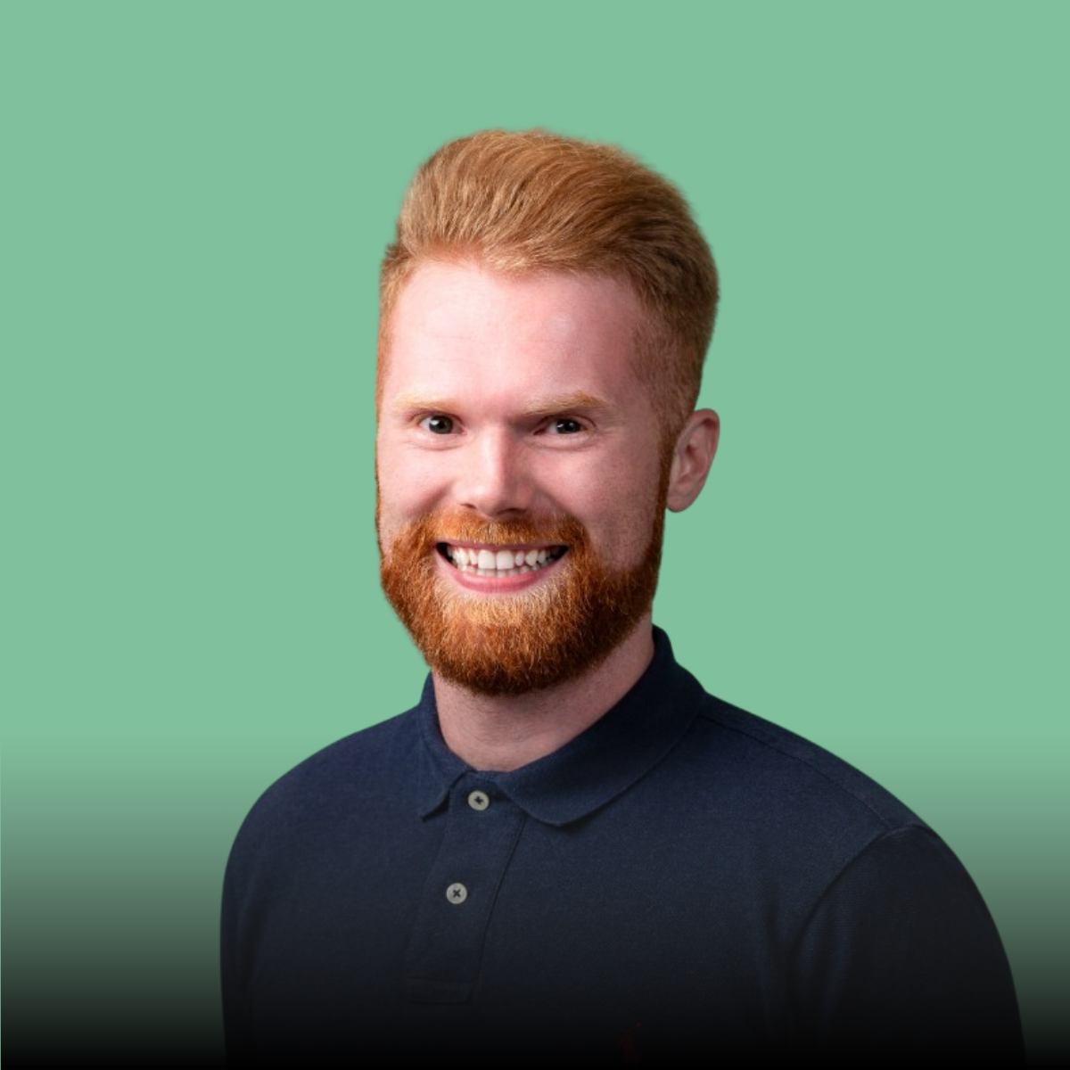 A man with a beard is wearing a blue polo shirt and smiling.