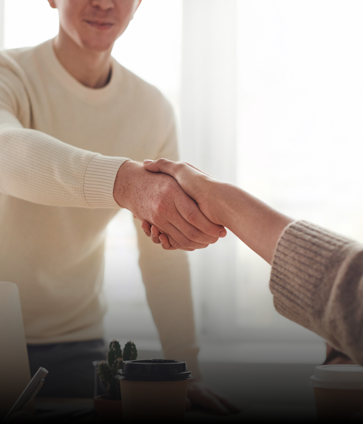 A man in a white sweater is shaking hands with a woman in a brown sweater.