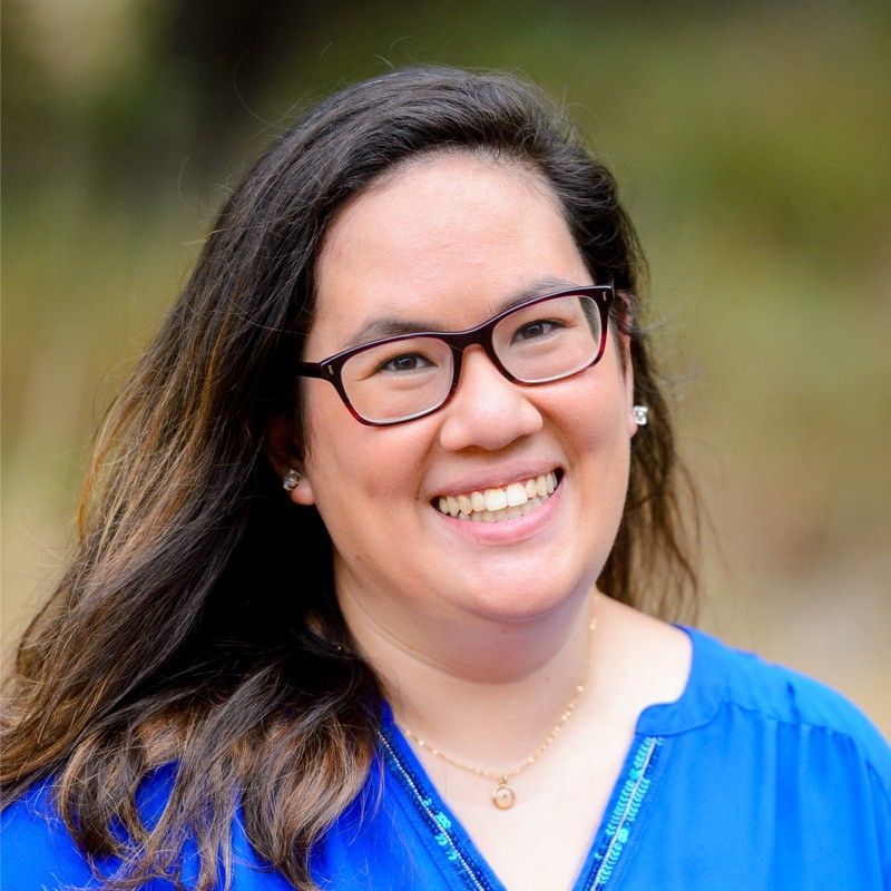 A woman wearing glasses and a blue shirt is smiling for the camera.