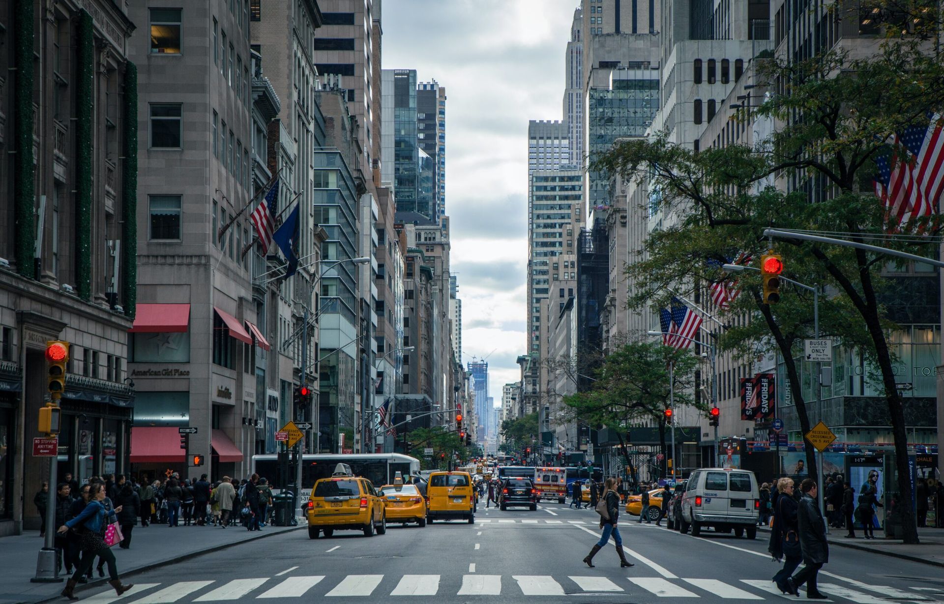 A busy city street with people crossing the street at a crosswalk.