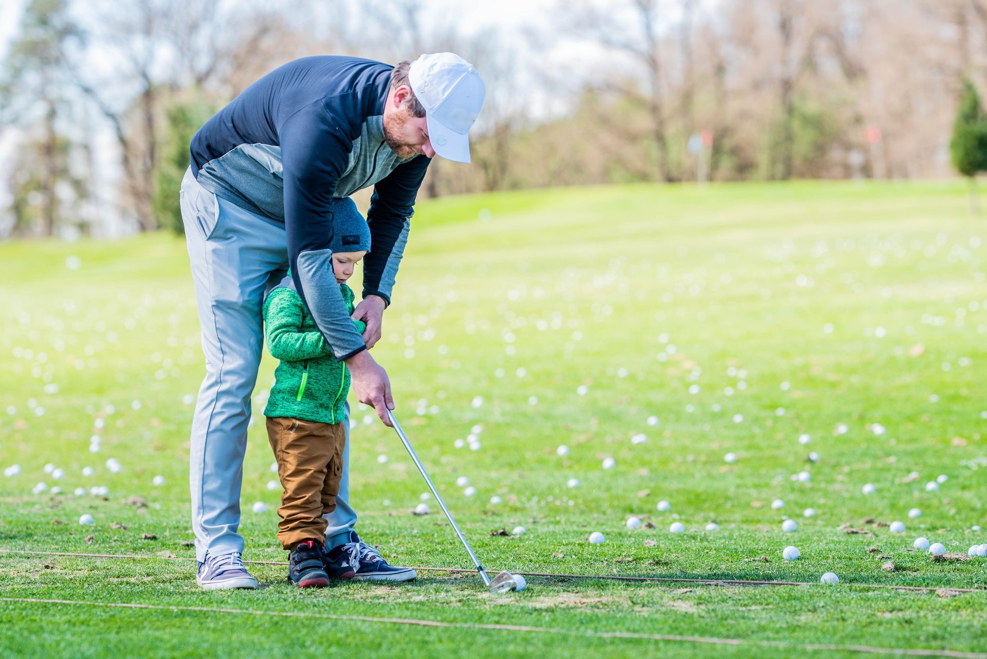 Man in white hat teaching a child to golf on a green golf course.