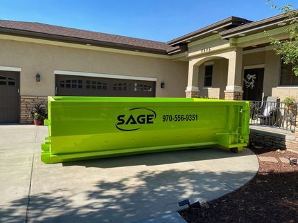 Green Sage dumpster in front of a house with a garage and porch on a sunny day.