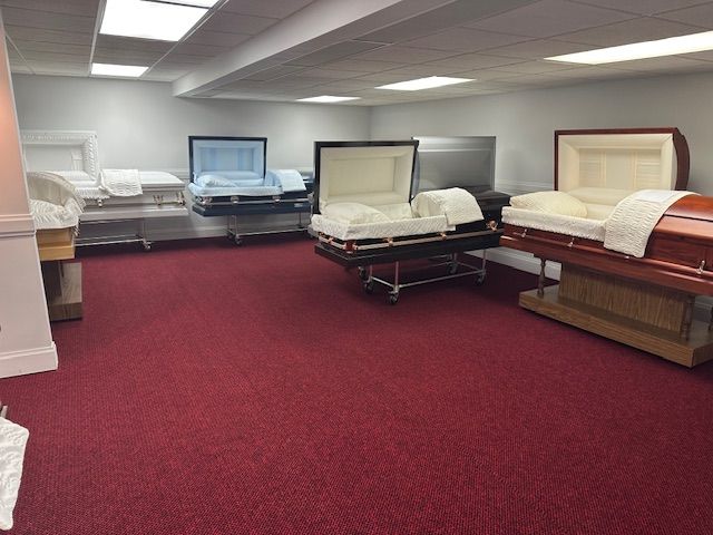 Interior of a funeral home showroom with several open caskets on display, red carpet floor.