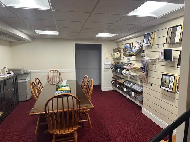 A small office with a conference table, chairs, displays of photos, and a copier. Red carpet and cream walls.