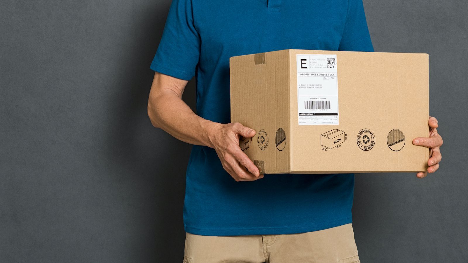 A man in a blue shirt is holding a cardboard box.
