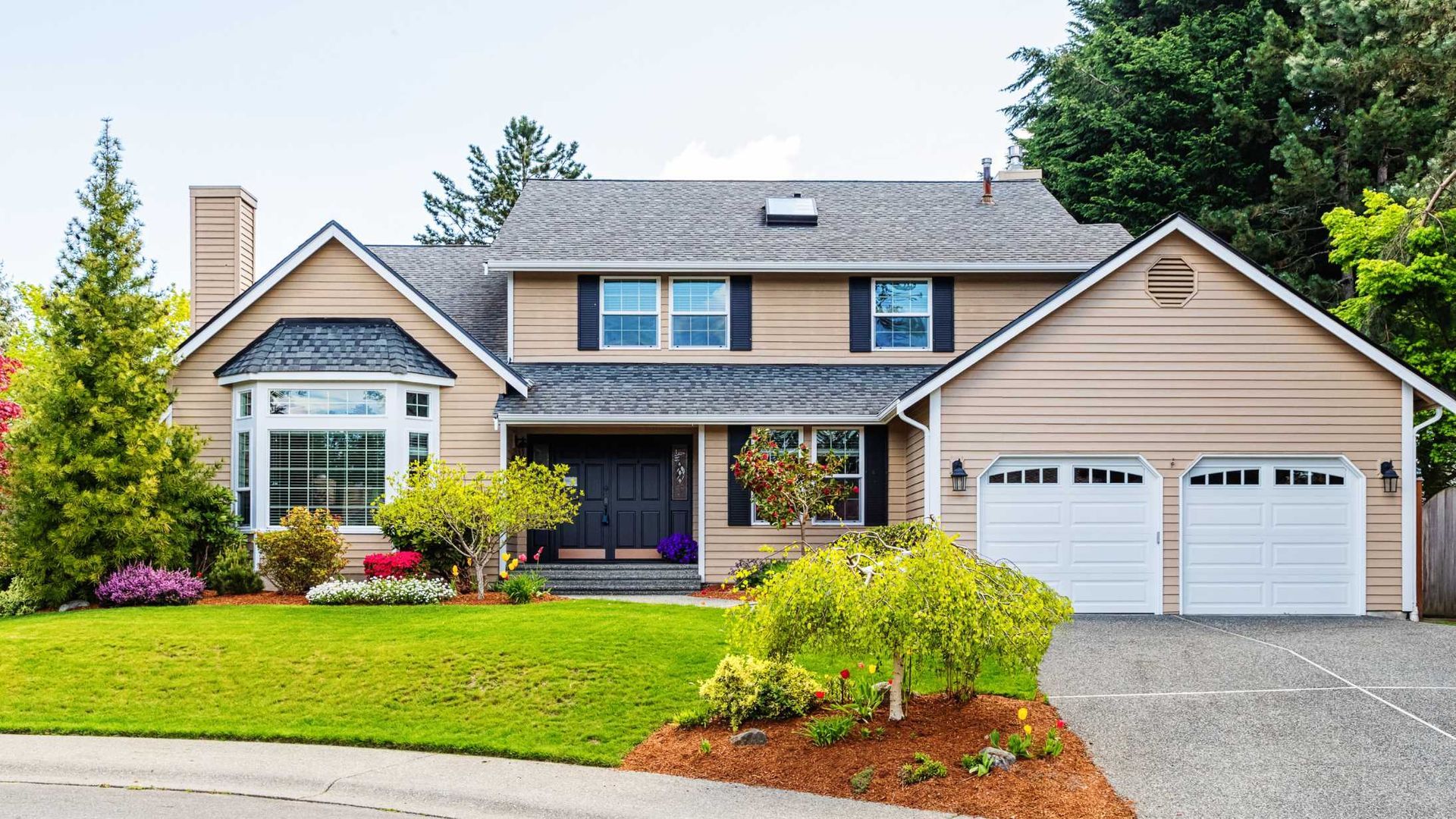 A large house with two garages and a lush green lawn.
