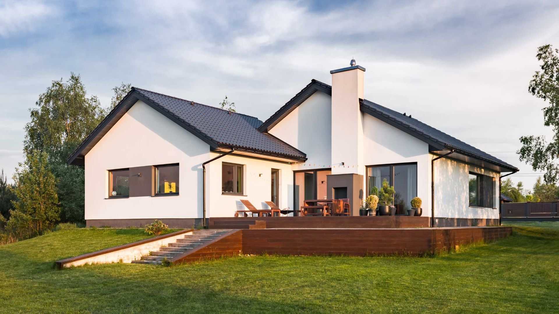 A large white house with a black roof is sitting on top of a lush green field.