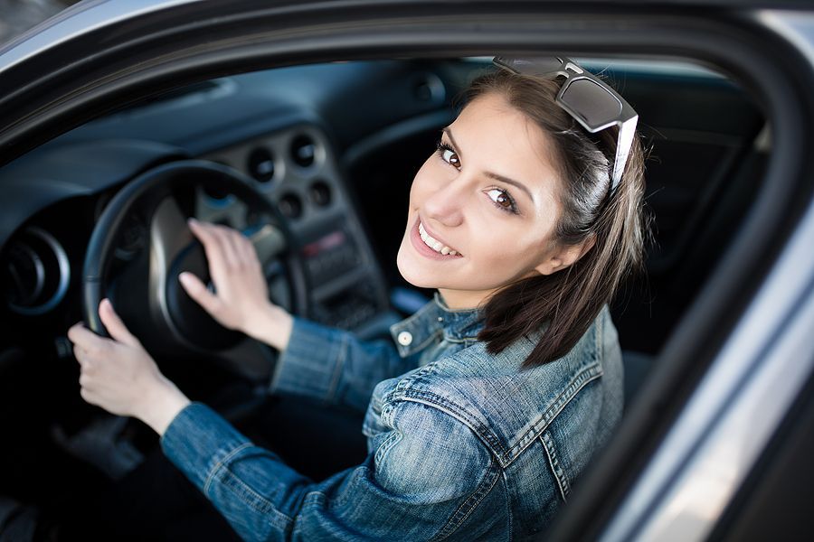 A woman is driving a car and smiling at the camera.