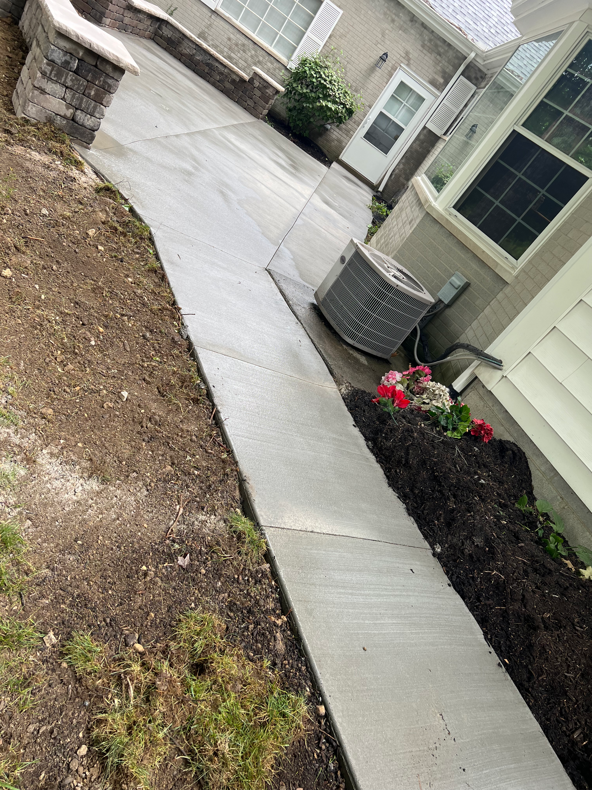 A concrete walkway leading to a house with a planter on the side of it.
