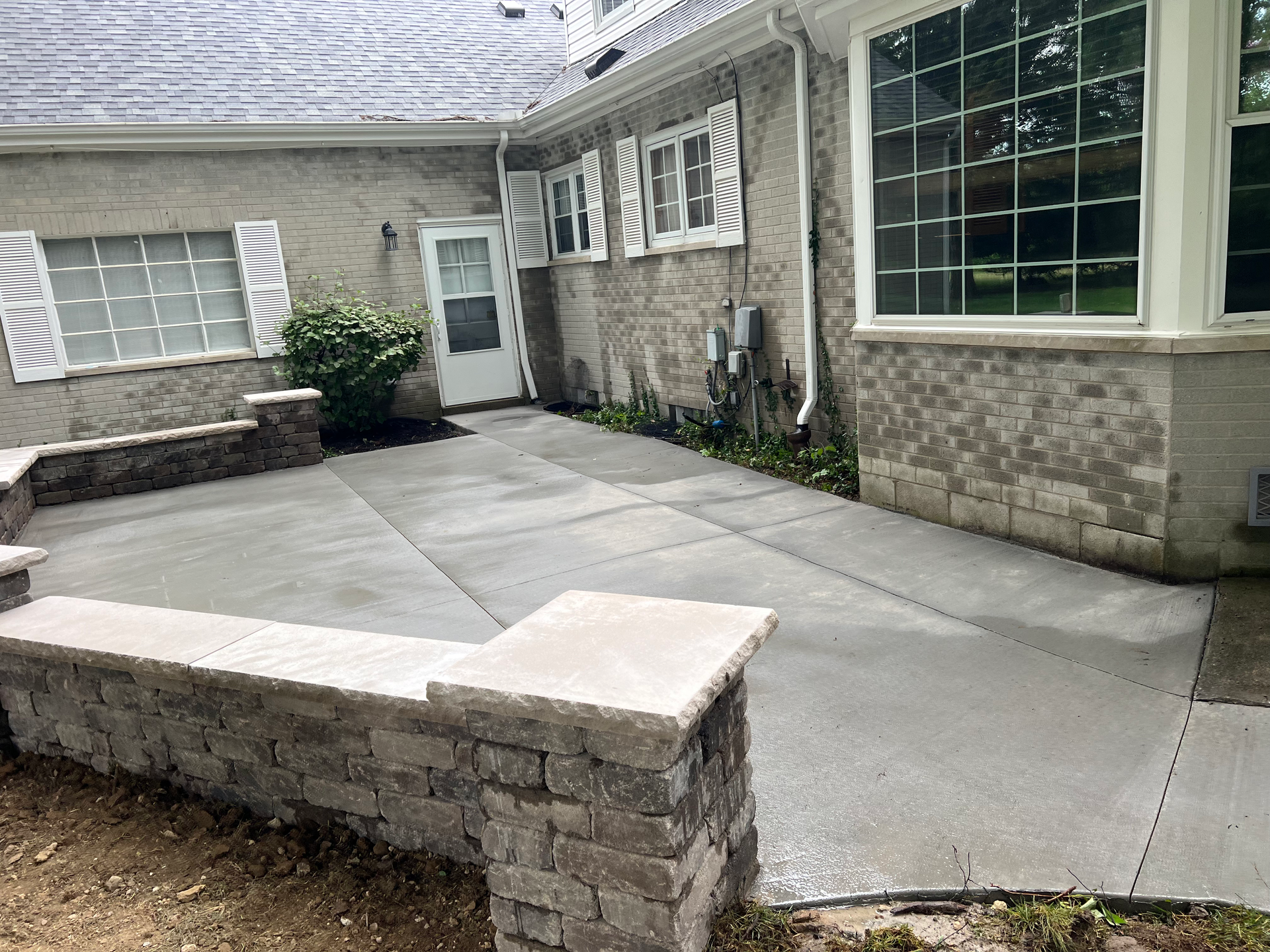 There is a concrete patio in front of a house with a brick wall.