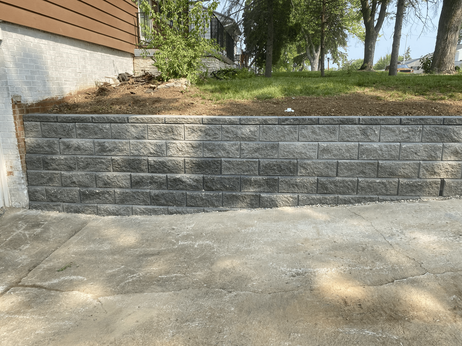 A brick wall is sitting on top of a concrete driveway next to a house.