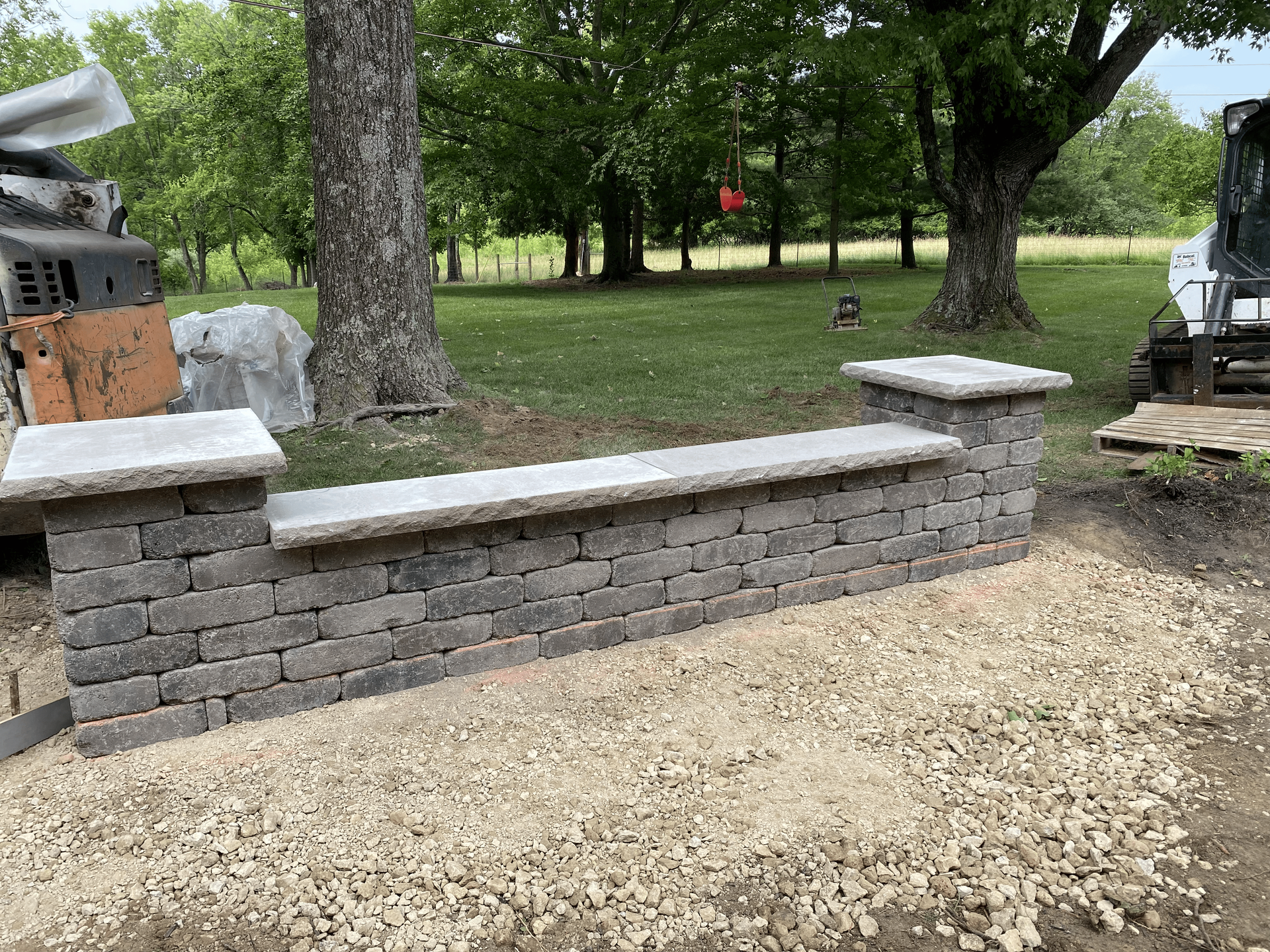 A brick wall is being built in a yard with trees in the background.