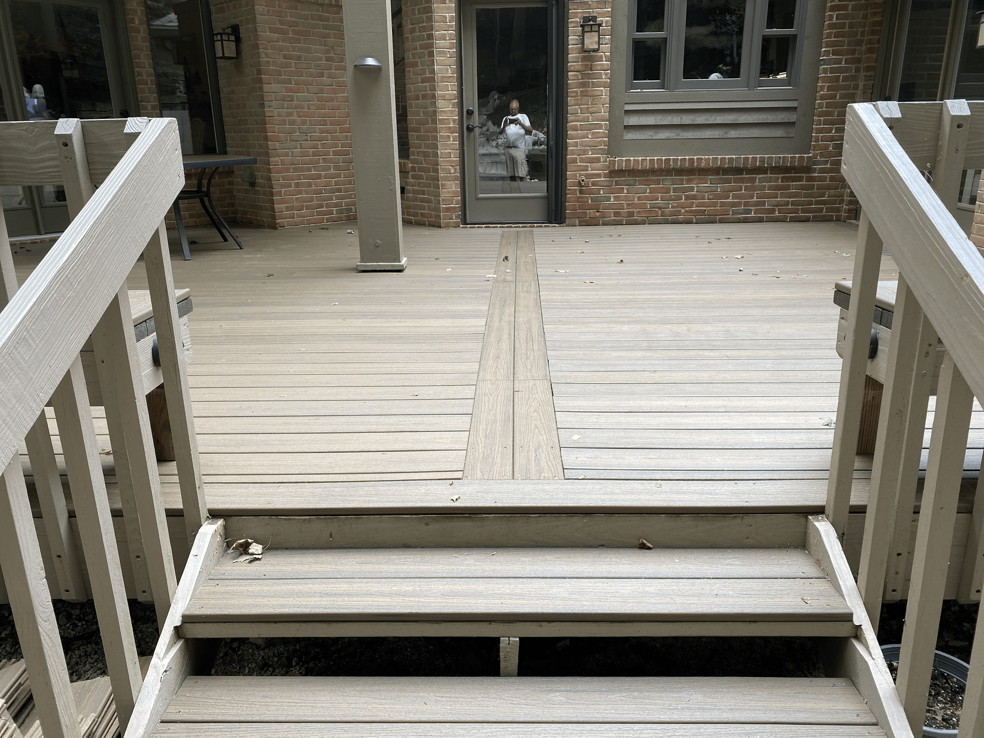 A wooden deck with stairs leading up to it and a brick building in the background.