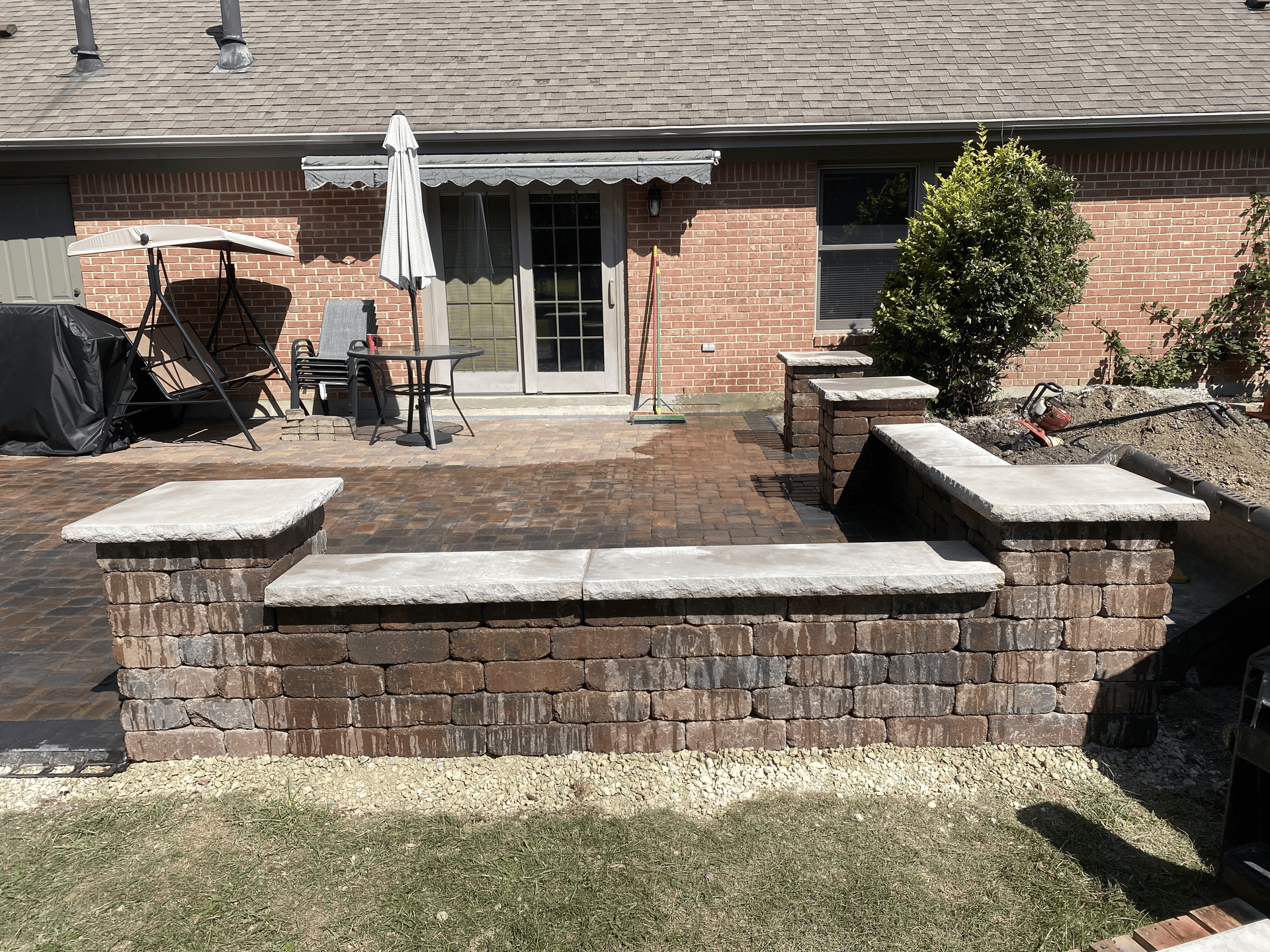 A brick patio with a bench and chairs in front of a brick house.