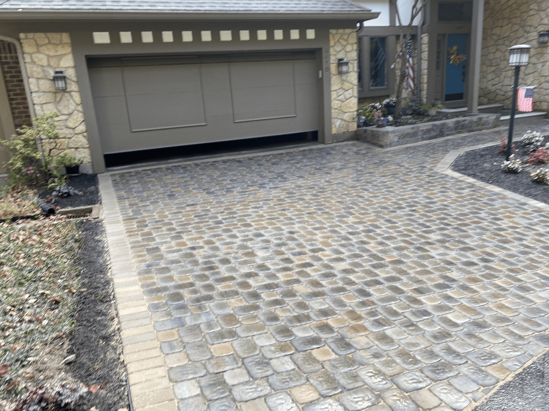 A cobblestone driveway in front of a house with a garage door.