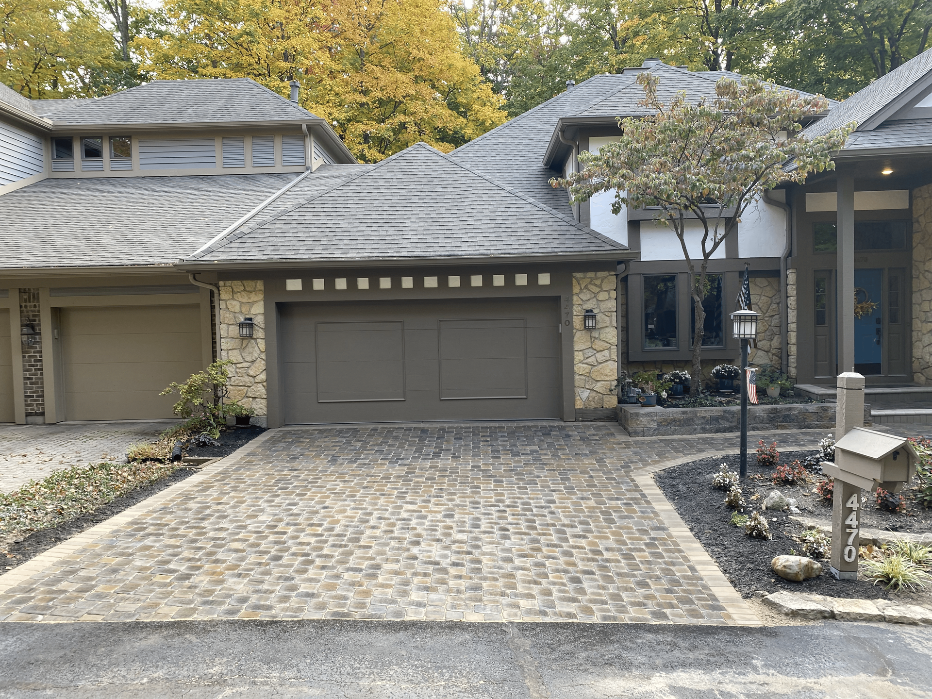 A large house with two garage doors and a brick driveway in front of it.