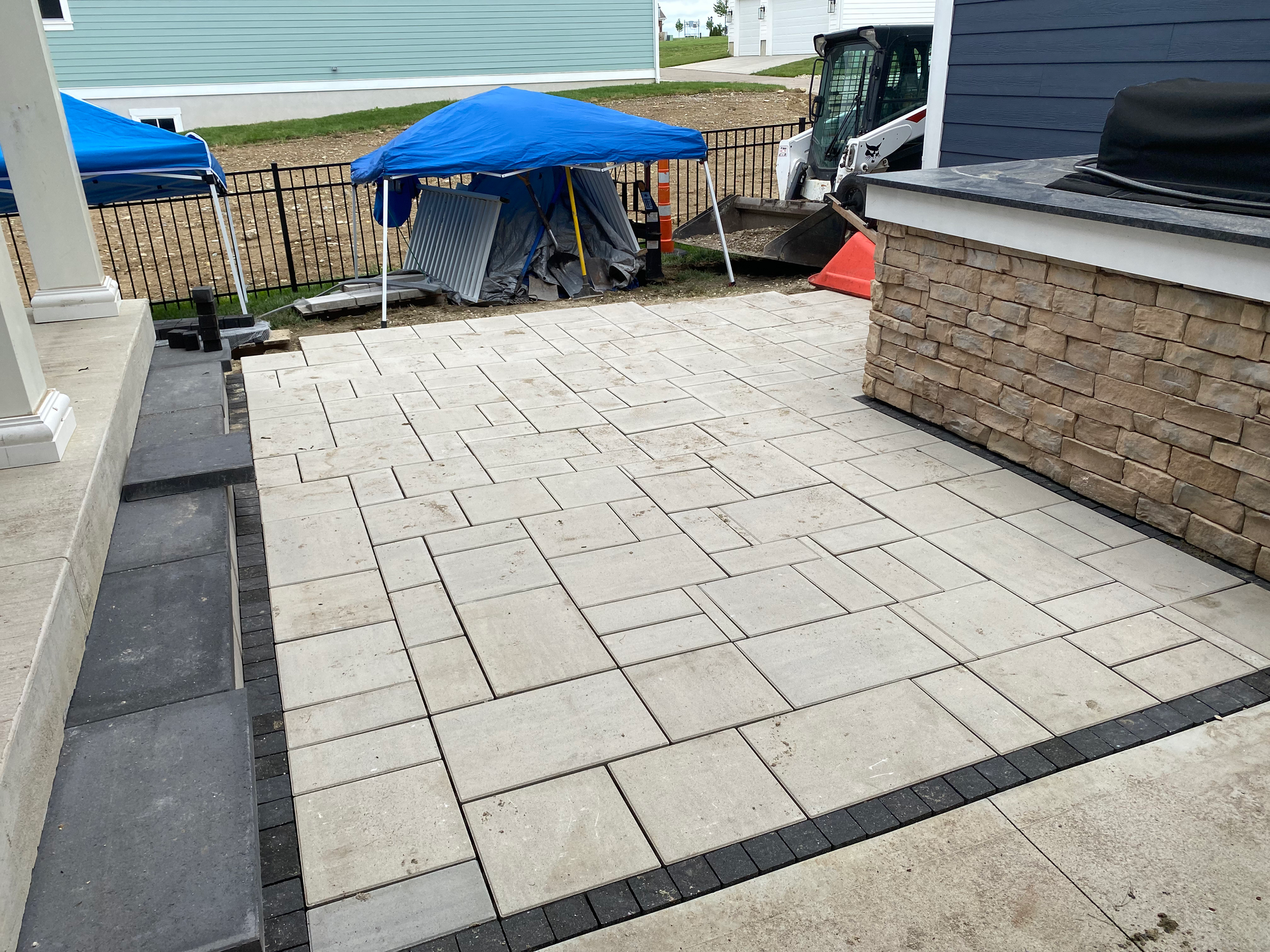 A patio with a blue tent and a grill in the background.