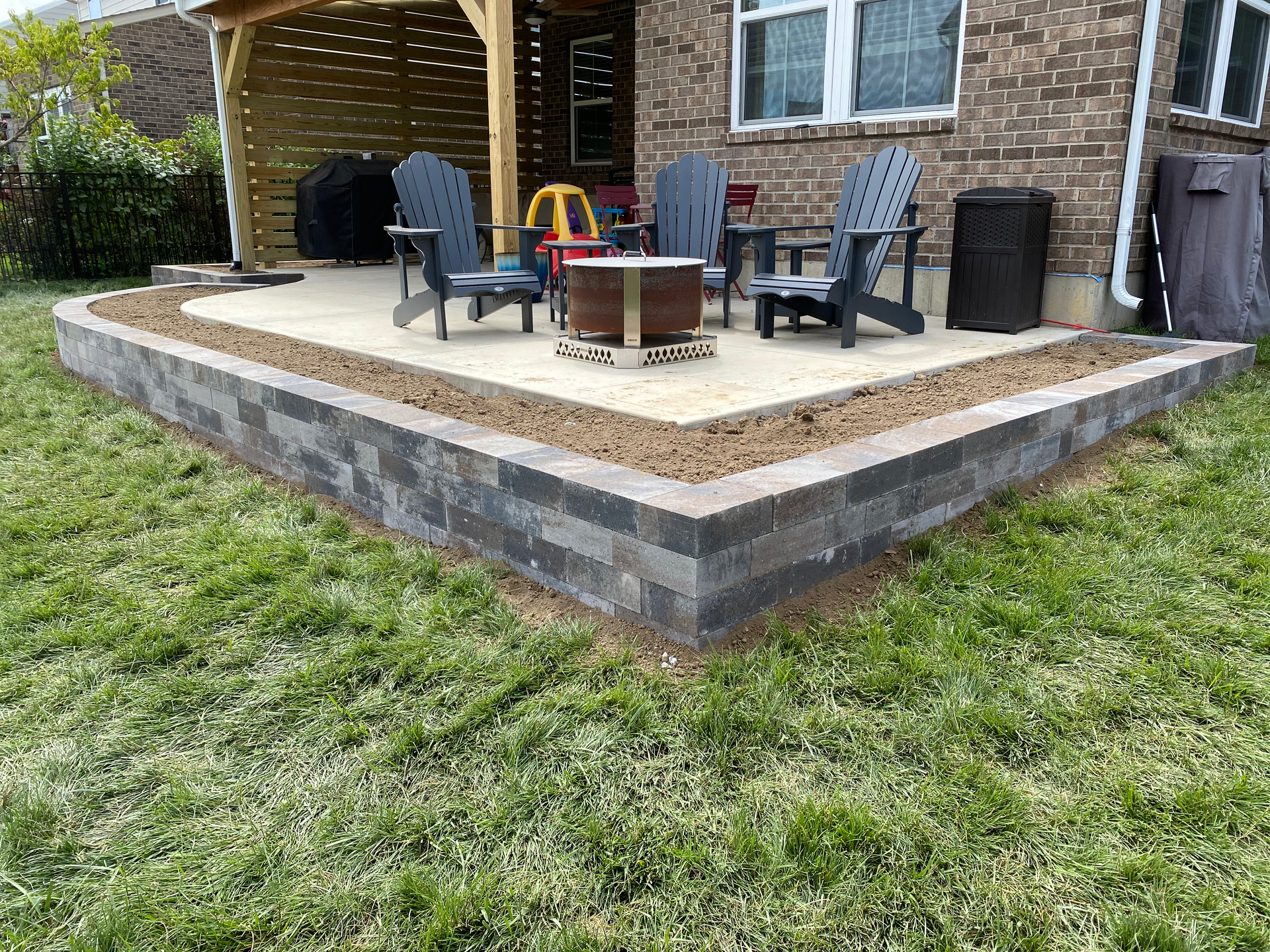 A patio with chairs and a fire pit in front of a brick house.