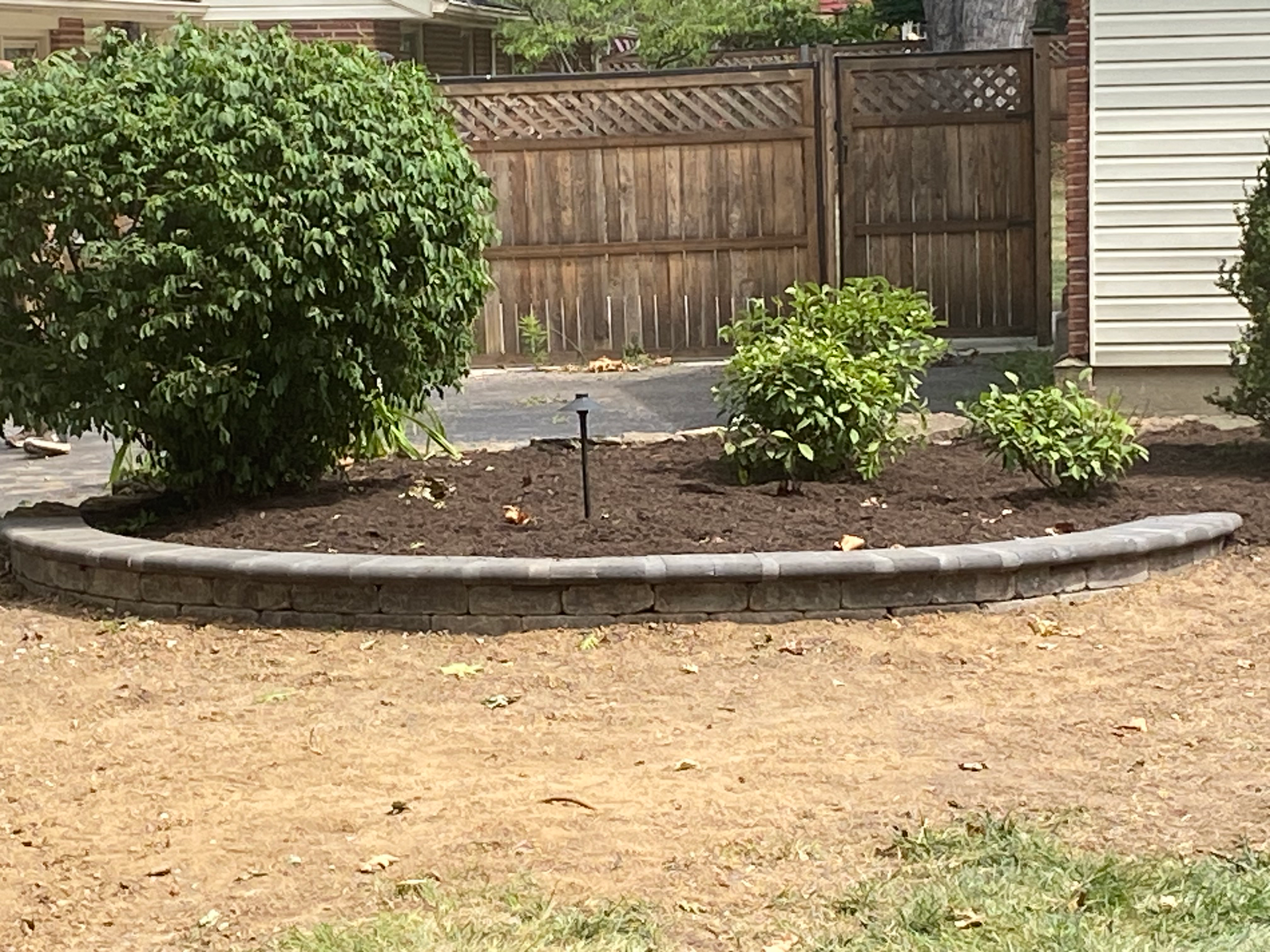 A garden in front of a house with a wooden fence in the background.