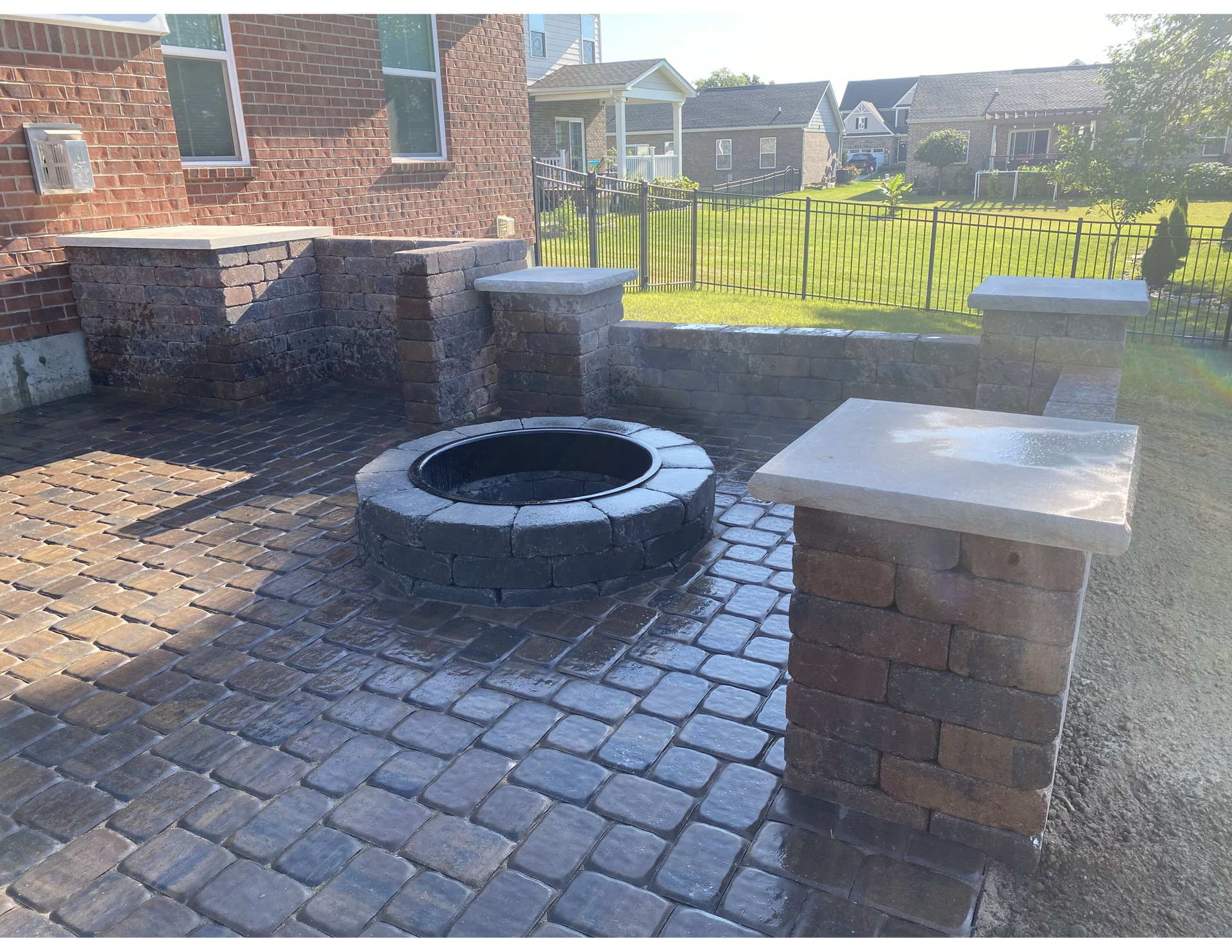 A fire pit is sitting on a brick patio in front of a brick house.