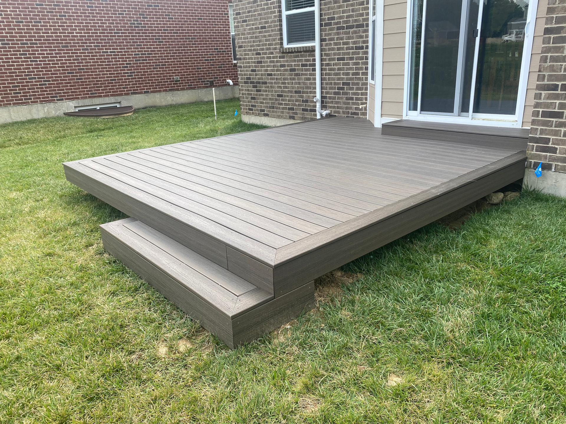 A wooden deck with stairs in front of a brick house.