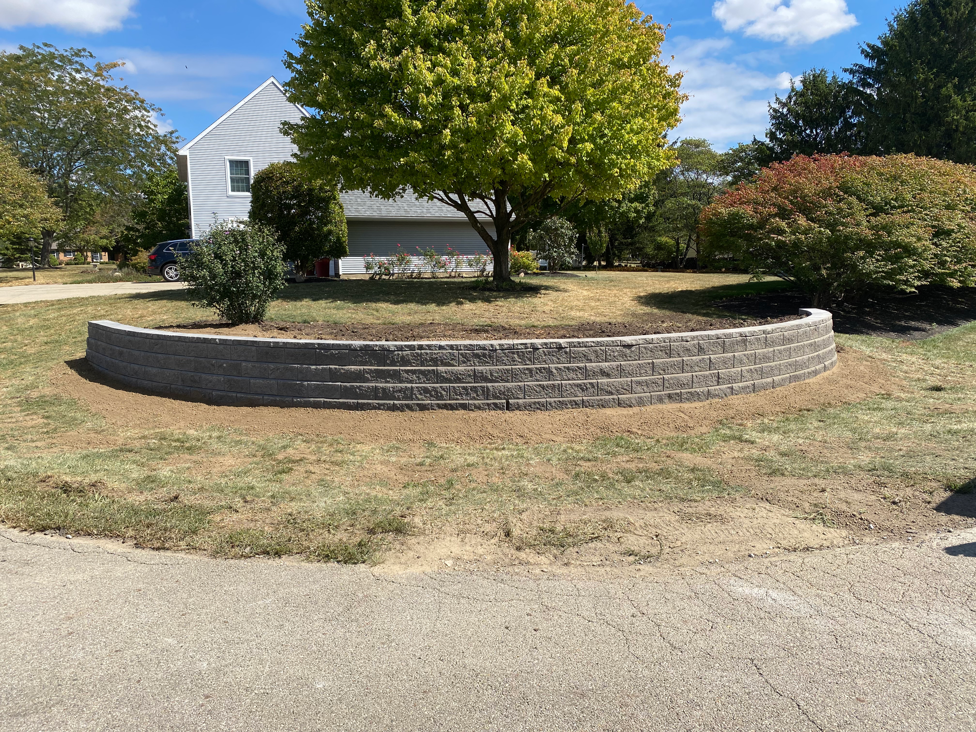 A brick wall is in the middle of a grassy field in front of a house.