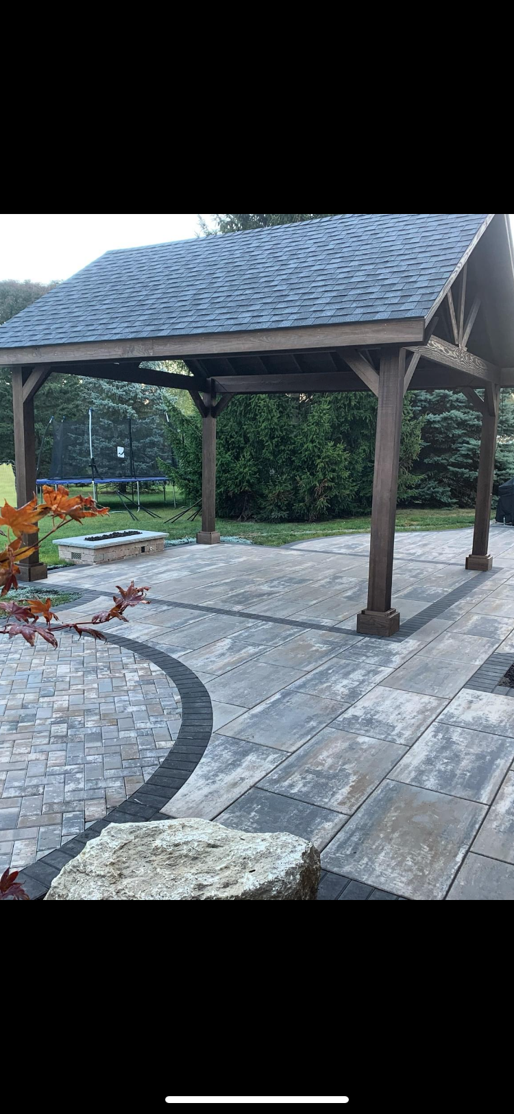 A wooden gazebo with a slate roof is sitting on top of a stone patio.