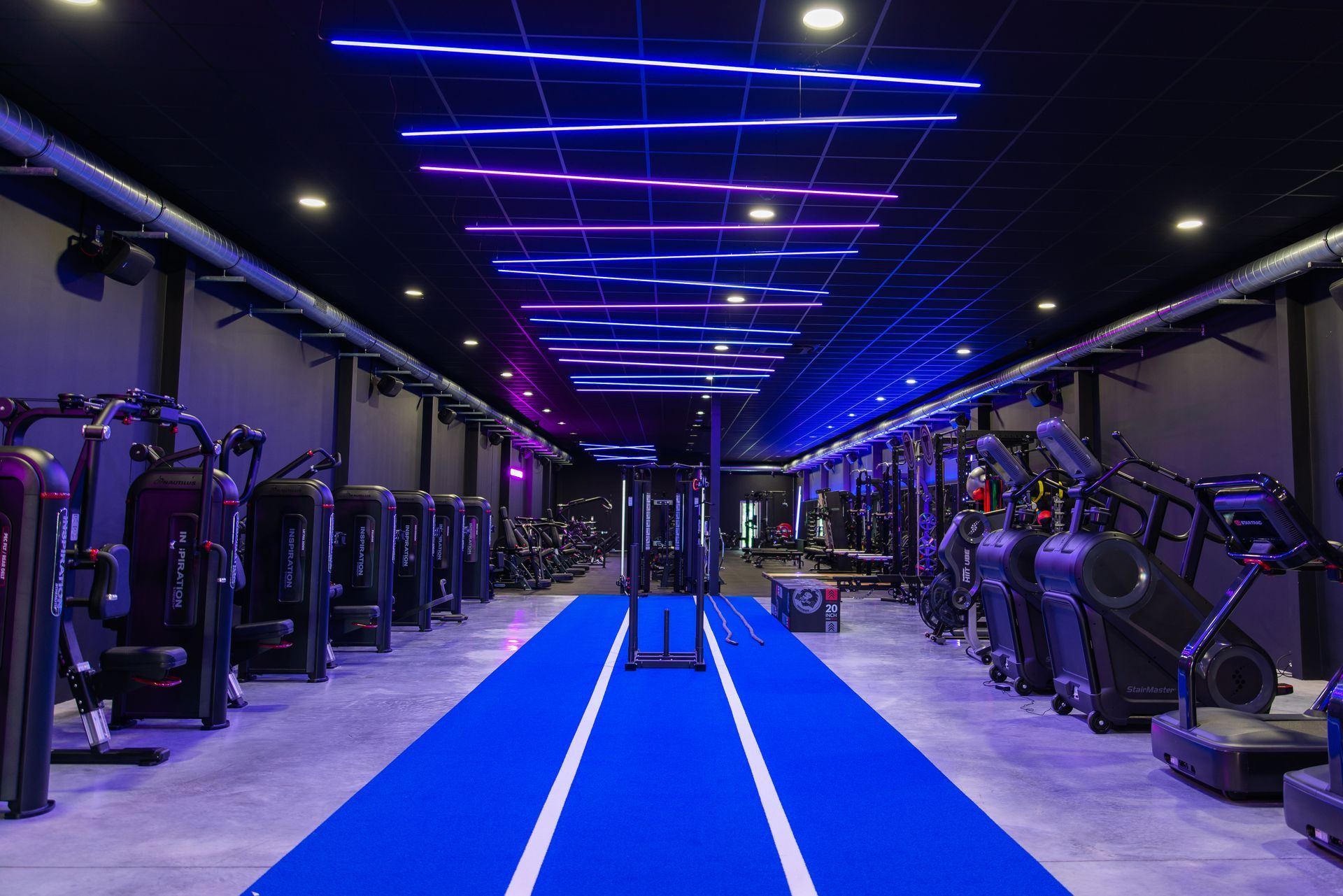 Een gymzaal vol met fitnessapparatuur en een blauwe baan.