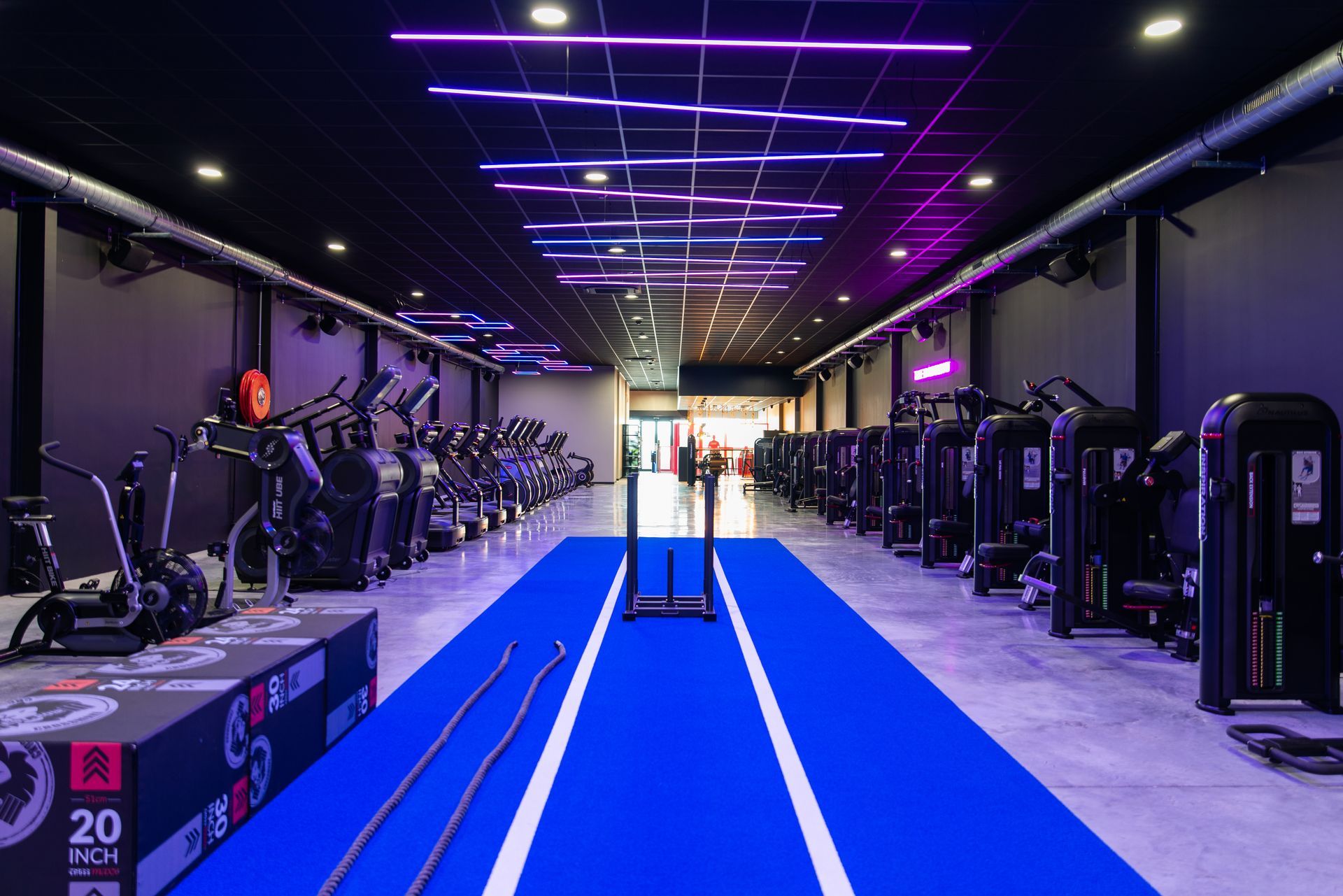 een sportschool vol met veel fitnessapparatuur en een blauwe mat.