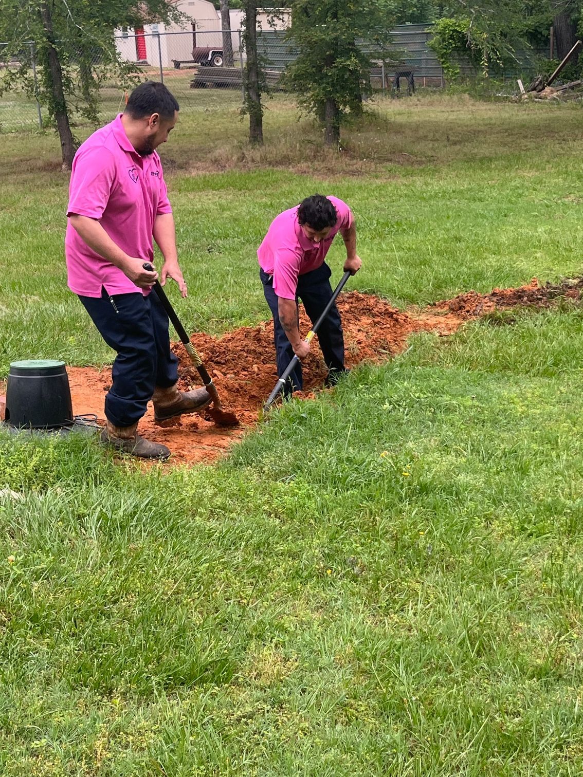 Two men are digging a hole in the grass with shovels.