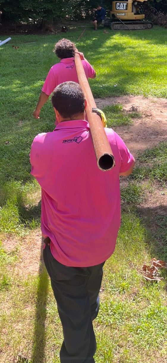 Two men in pink shirts are carrying a large pipe on their shoulders.