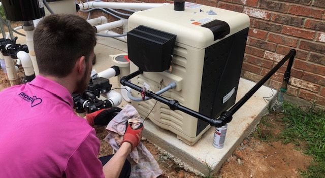 A man in a pink shirt is working on a pool heater.