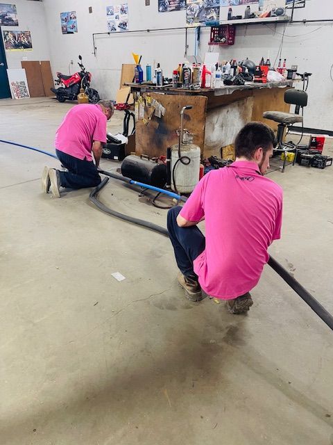 Two men in pink shirts are working in a garage