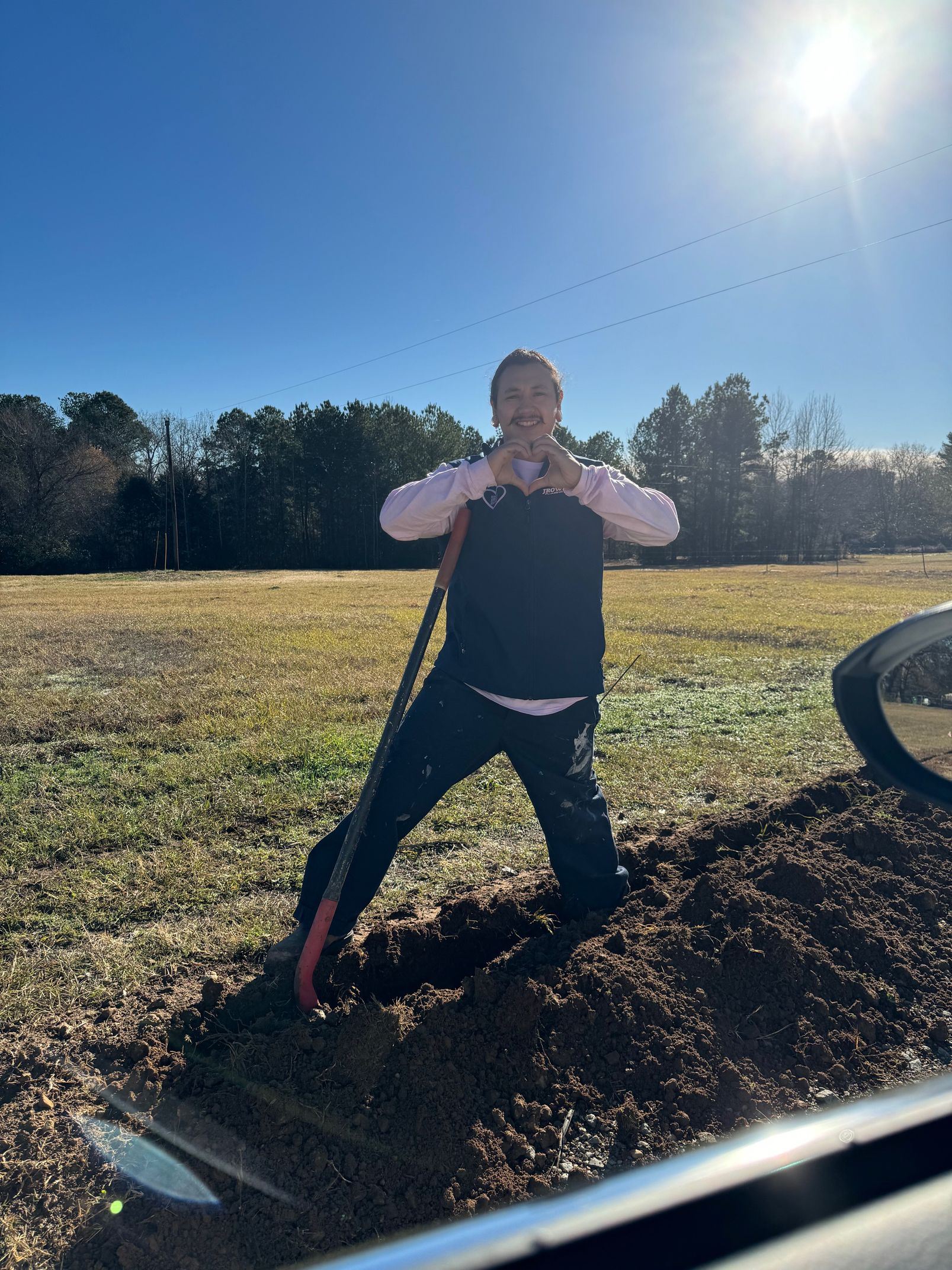 A person is standing in the dirt with a shovel in a field.