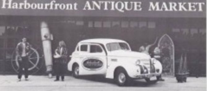 A white car is parked in front of the harbourfront antique market