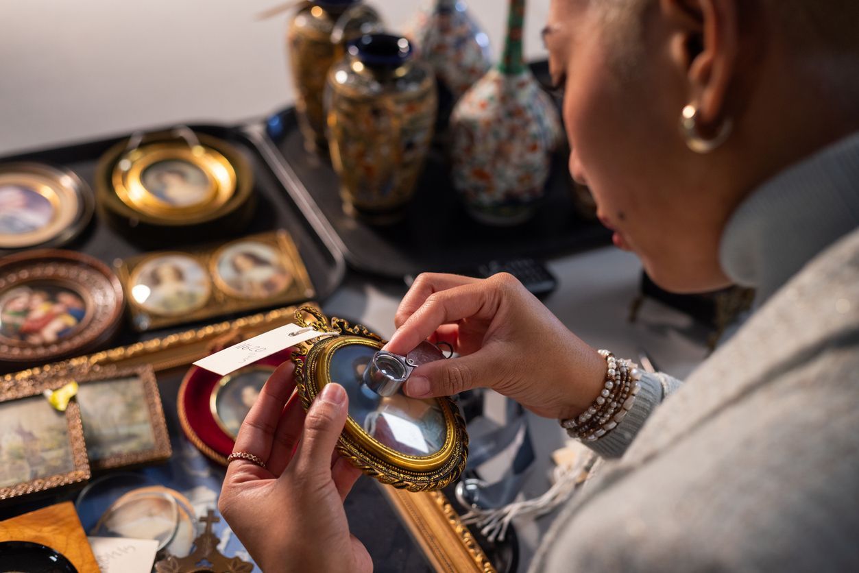 A woman is looking at a picture frame with a magnifying glass.