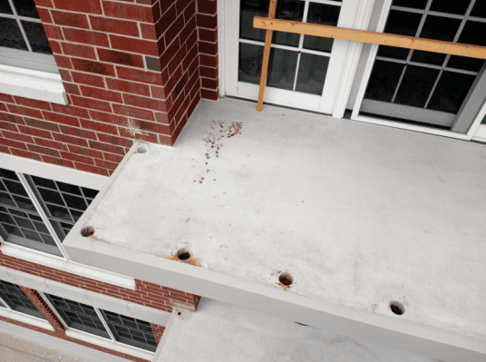 Close-up view of a concrete balcony with exposed anchor holes and signs of rust staining