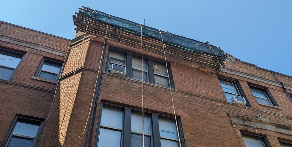Brick building with metal scaffolding above windows, against a blue sky.