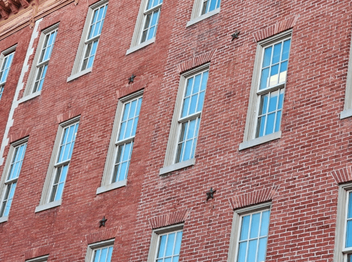 A close-up of a red brick building exterior featuring vertical rows of tall, rectangular windows with light frames.