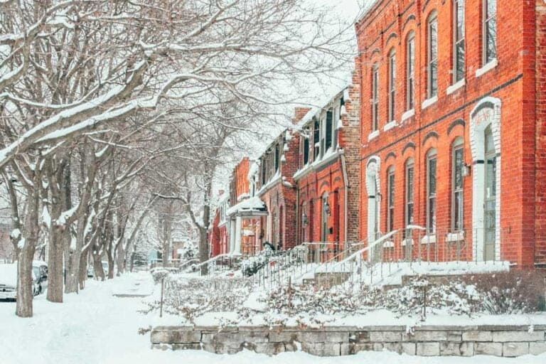 A row of red brick houses covered in snow along a street lined with snow-covered trees.