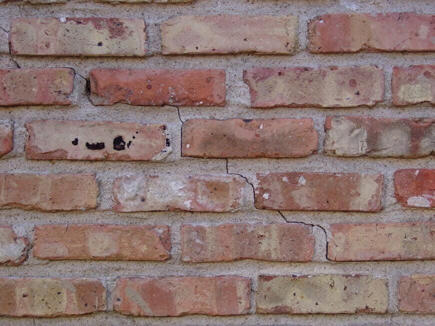 Close-up of a rustic brick wall with visible mortar joints and a diagonal crack running through several bricks.