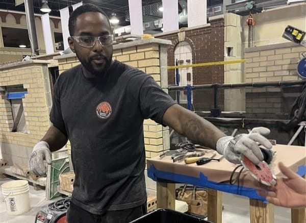 International Masonry Institute trainer holding a diamond sandwich tuckpointing blade, used for precise mortar joint removal during masonry restoration and repointing work.