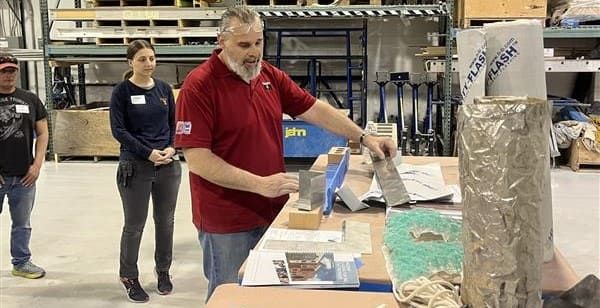 Instructor demonstrating components of a complete masonry flashing system, including stainless steel drip edge, end dams, weeps, and flexible flashing membrane, during a hands-on training workshop focused on moisture management in masonry walls.
