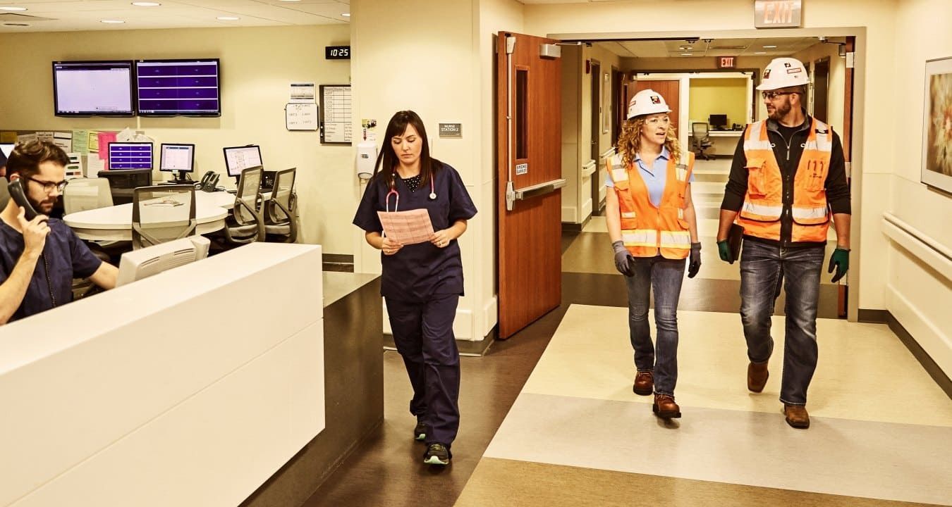 Construction professionals walking through a hospital corridor alongside medical staff